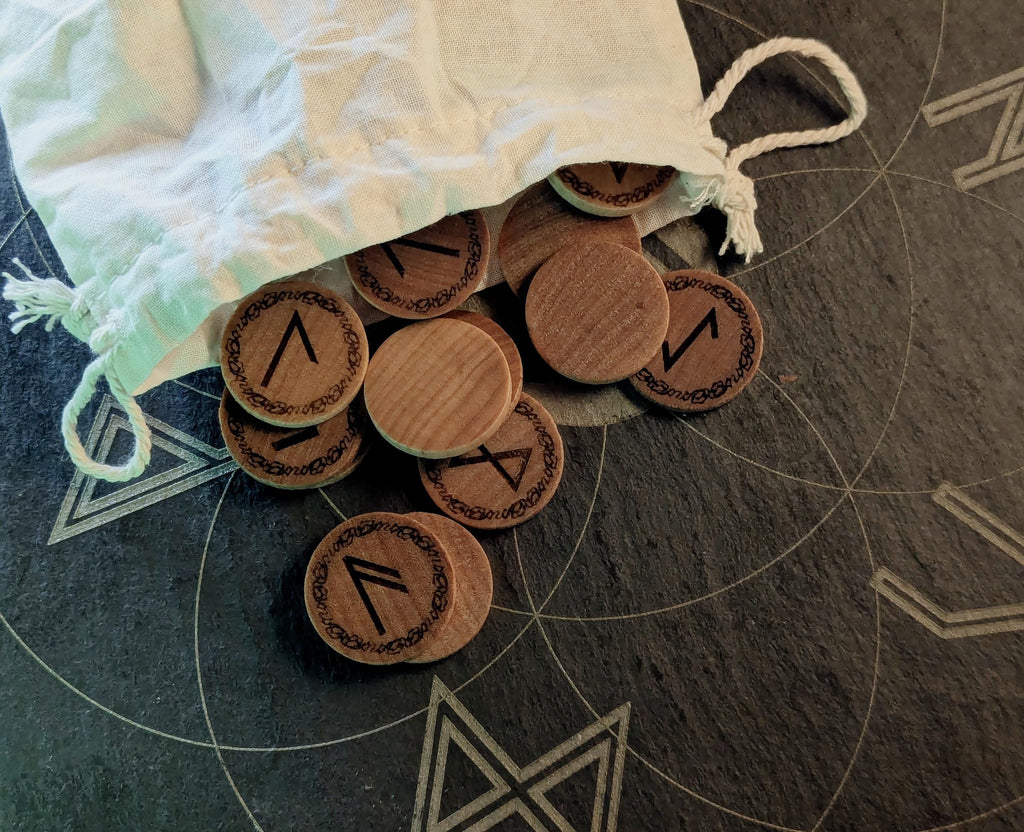 Elder Futhark Rune Set, hadcrafted from hardwood in Canada, on a stone surface with a drawstring bag.