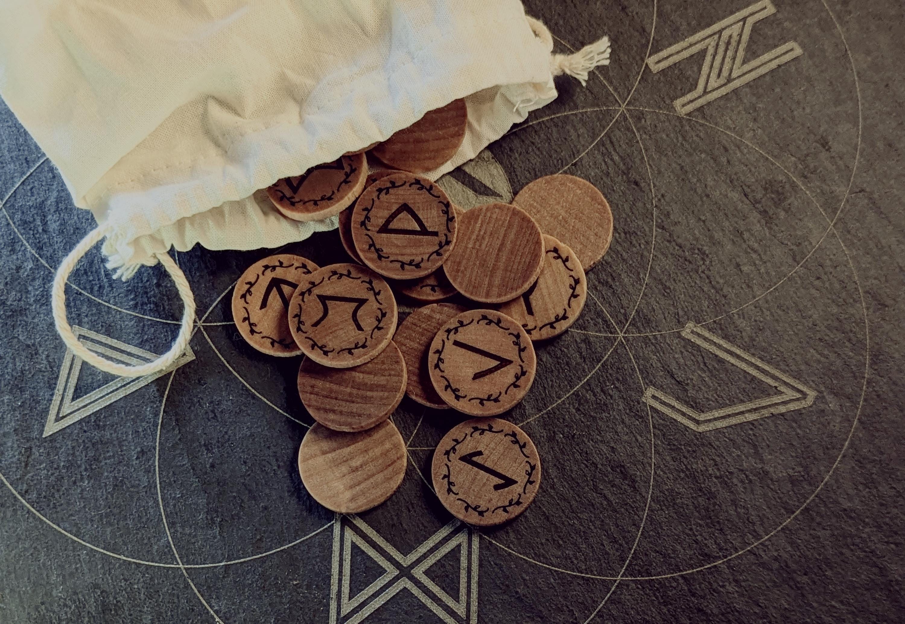 Elder Futhark Rune Set, hadcrafted from hardwood in Canada, on a stone surface with a drawstring bag.